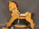 yellow wooden rocking horse with brown mane on wheels on a gray background