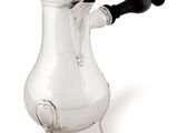a silver coffee pot with a black handle on a stand