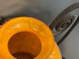 an orange vase with a leaf handle on a stand