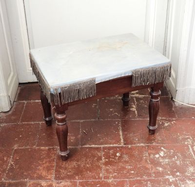 un petit banc orné de franges, placé dans un coin de la pièce