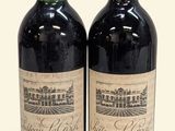 two bottles of red wine sitting next to each other on a white surface