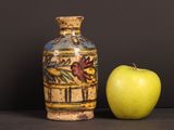 an apple next to a vase with a painting on it