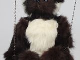 un ours en peluche assis sur une balançoire, avec un cœur sur la poitrine