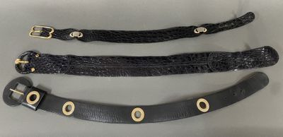 three black leather belts with gold buckles on a gray surface
