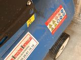 a blue air compressor sitting on the floor next to a brick wall