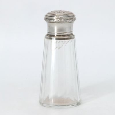 une salière en verre avec un couvercle argenté, posée sur une surface blanche