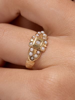 a woman ' s hand holding a gold ring with pearls on it