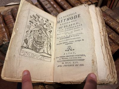 une personne tient un vieux livre à la main devant une pile de vieux livres