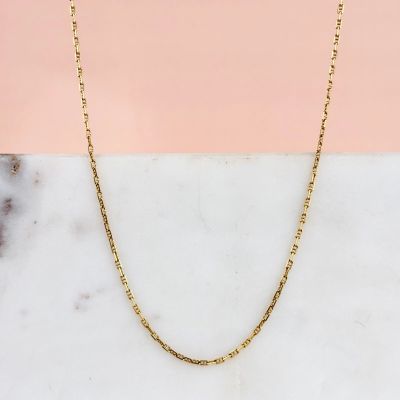 un collier à chaîne en or posé sur une surface en marbre