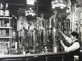 black and white photograph of a woman standing at a bar in front of a bunch of bottles