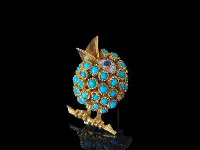 un gros plan d'une broche en or et turquoise posée sur une surface noire