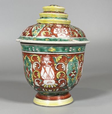 un vase orange, vert et blanc muni d'un couvercle, posé sur un socle