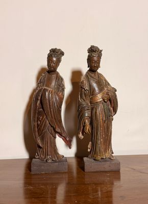 une paire de figurines asiatiques posées sur une table en bois, avec un mur blanc en arrière-plan