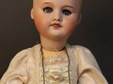 a doll that is wearing a white dress and a necklace