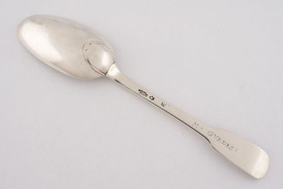 cuillère en argent portant une inscription, posée sur une surface blanche