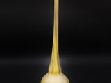 un vase jaune à long pied posé sur une surface noire