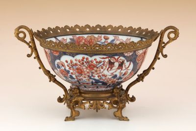 un grand bol décoré posé sur un socle, sur une surface blanche