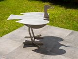 a metal sculpture of a bird on a table in the grass