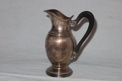 a silver pitcher with a black handle sitting on a table