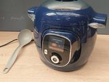 a blue electric pressure cooker with a spoon next to it