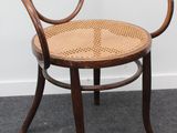 une photo d'une chaise en bois avec une assise tressée, posée sur un sol recouvert de moquette
