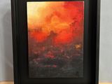 un tableau représentant un coucher de soleil orange et rouge dans un cadre noir