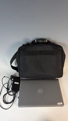 un ordinateur portable Dell avec son chargeur et sa sacoche, posé sur une table blanche