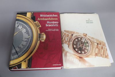 deux livres posés sur une table, avec une montre dessus, et une autre montre posée par-dessus