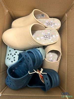 Plusieurs paires de Crocs se trouvent dans une boîte en carton posée par terre.