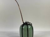 a green vase with a bamboo stick sticking out of it