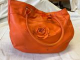 un sac à main orange orné d'une rose, posé sur un lit