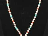 a necklace with a turquoise and red stone pendant on a black mannequin
