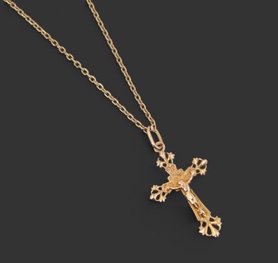 un pendentif en forme de croix en or, suspendu à une chaîne, sur fond noir