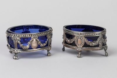 une paire de bols en verre argenté et bleu, posés sur des socles, sur une surface blanche
