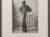 une vieille photo en noir et blanc d'une femme appuyée contre une chaise