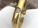 a gold ring with a watch on it sitting on top of a piece of wood