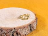 bague plaquée or posée sur un support en bois, sur fond jaune