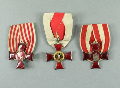 three medals are displayed on a gray surface with a red and white striped ribbon