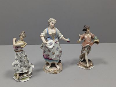 trois figurines en porcelaine représentant des femmes en robe et chapeau, posées sur une table