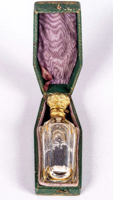 un petit flacon de parfum dans un étui vert posé sur une surface blanche