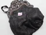 un vieux sac à main noir orné d'un autocollant rose, posé sur une surface blanche