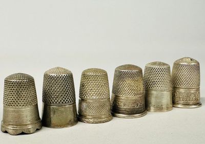 six antique thimbles lined up in a row on a white surface