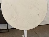 an image of a round table with a white base and a black chair in the background
