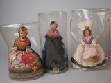 three glass vases with dolls in them sitting on a table