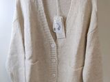 un cardigan beige suspendu à un cintre sur un mur blanc