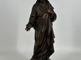 statue en bronze représentant un homme tenant une croix, posée sur un socle