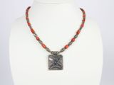 un collier avec un pendentif carré et des perles rouges sur un mannequin