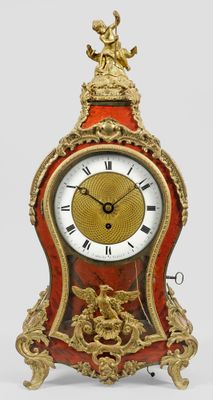 a red and gold clock sitting on a white surface
