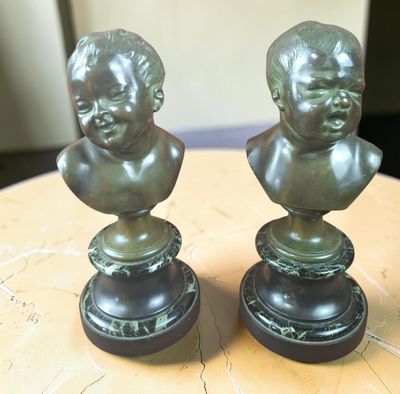 paire de bustes d'enfants en bronze sur socle, posés sur une table en bois