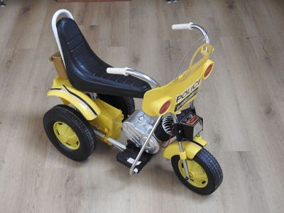 un petit tricycle jaune avec un siège noir posé sur un plancher en bois
